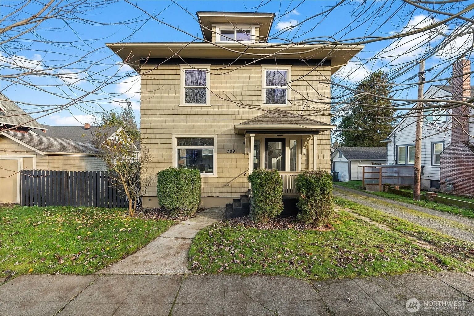 Two-story beige house with a small porch, surrounded by a lawn and bare trees.