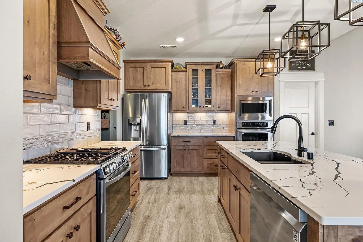 Modern kitchen with wooden cabinets, stainless steel appliances, marble countertops, and pendant lighting.