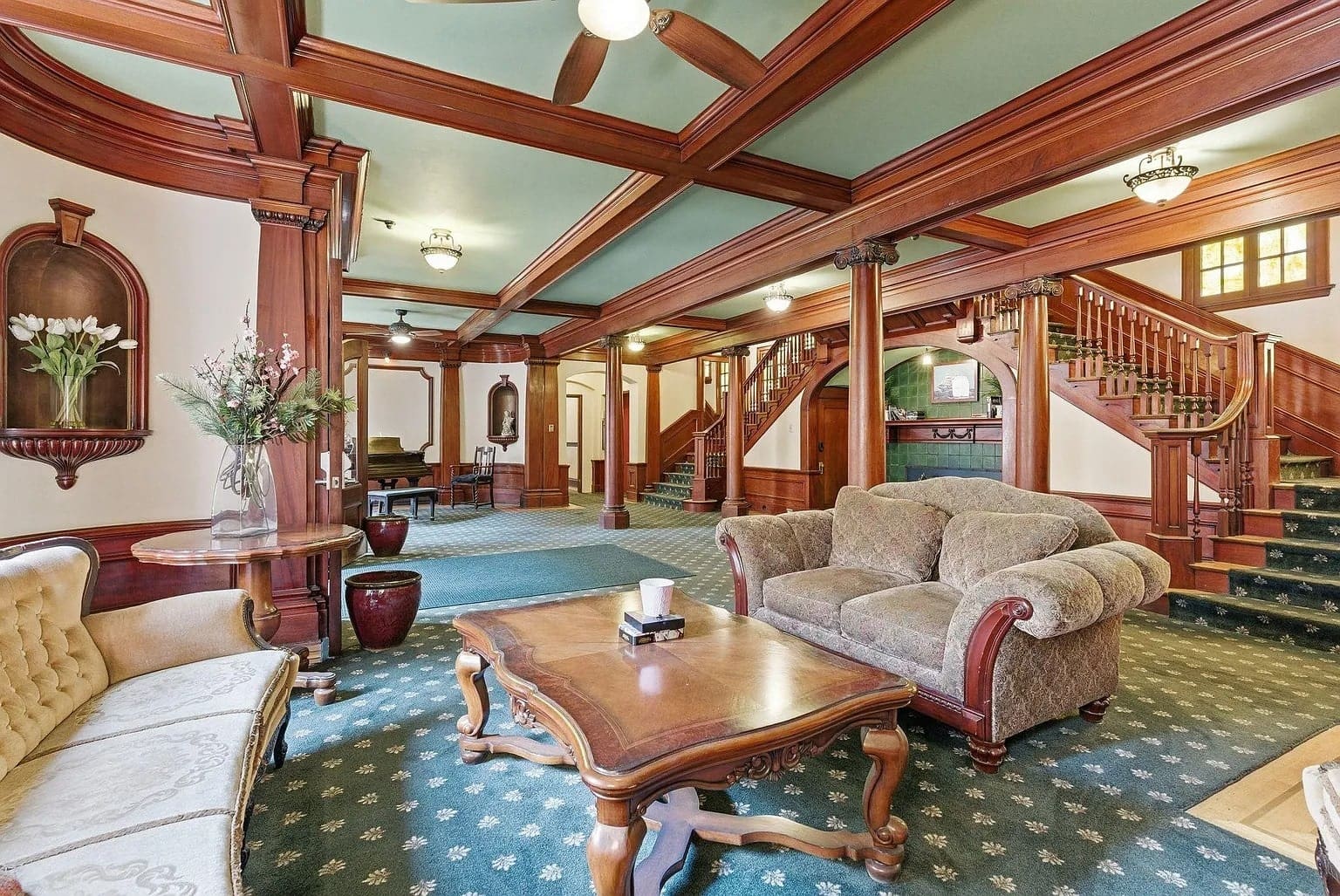 Elegant vintage-style living room with wooden beams, plush sofas, and a staircase in the background.