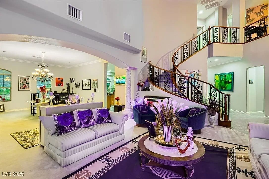 Luxurious living room with elegant furniture, ornate staircase, and vibrant artwork on the walls.