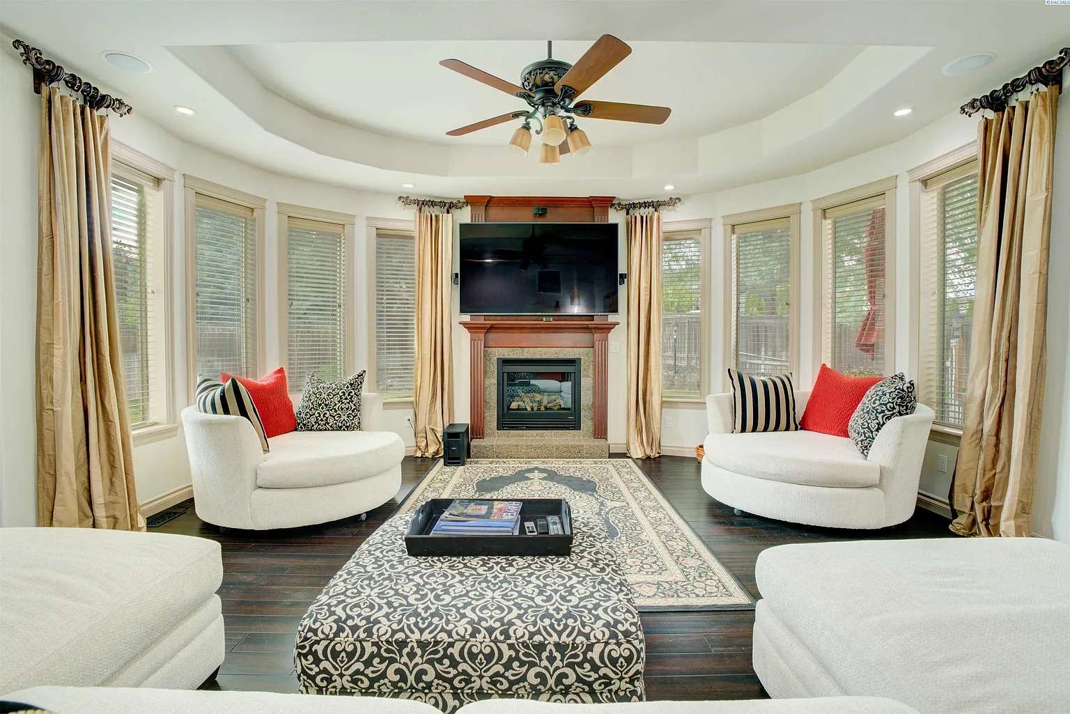 Spacious living room with circular sofas, fireplace, TV, and large windows with curtains.