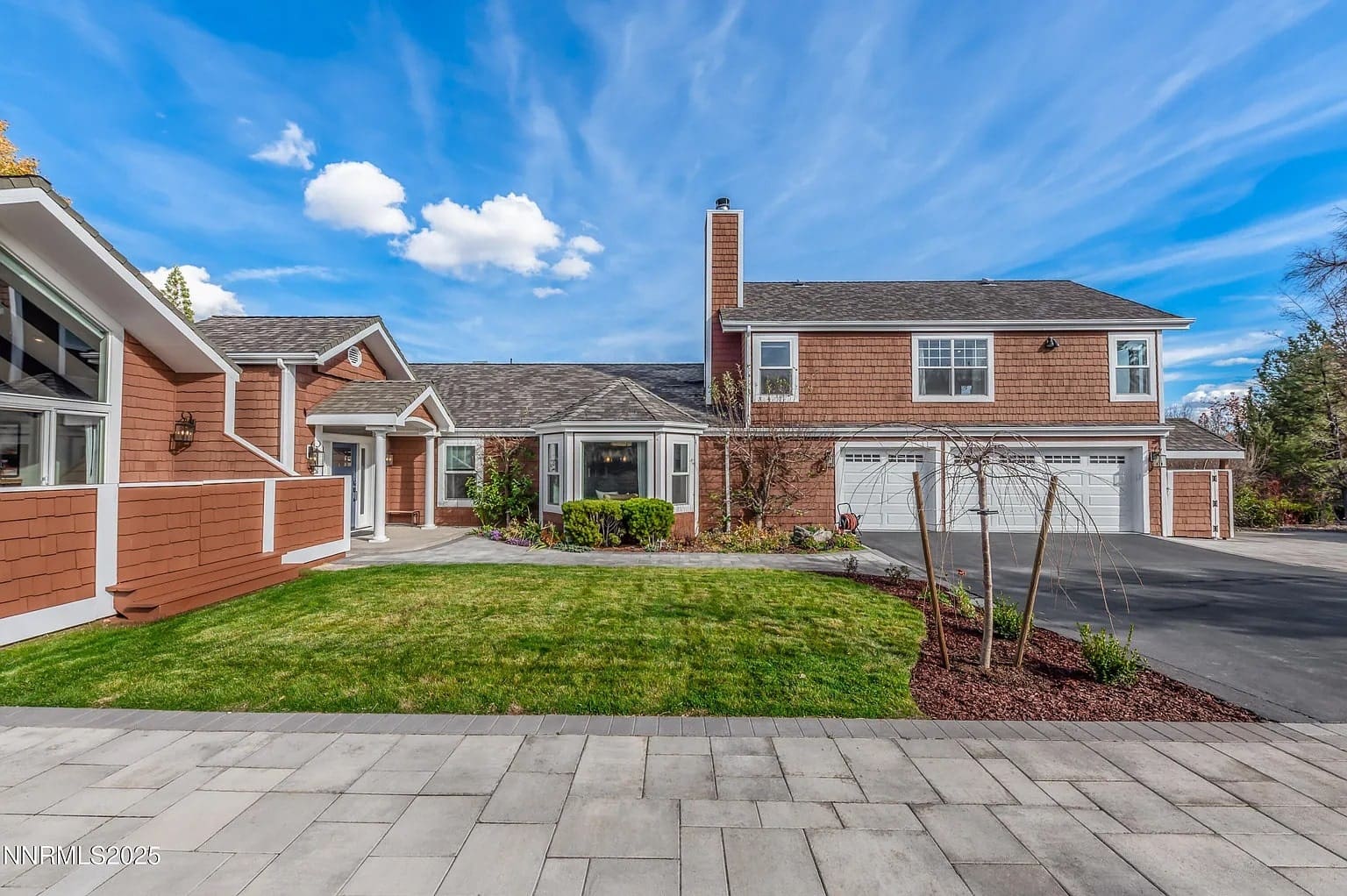 Spacious suburban house with brown siding, large driveway, and well-maintained lawn under a blue sky.