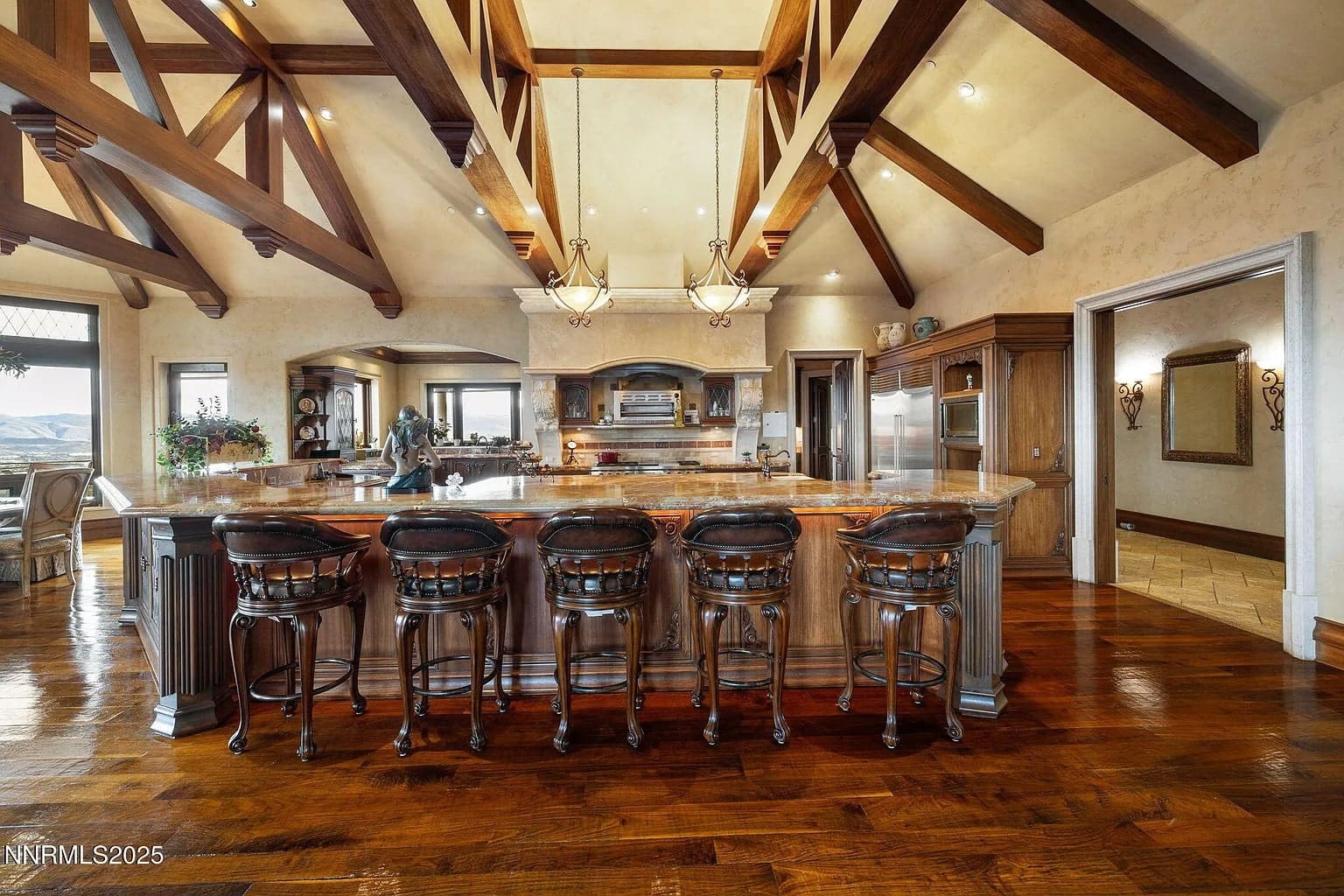 Spacious kitchen with wooden beams, large island, bar stools, and modern appliances.