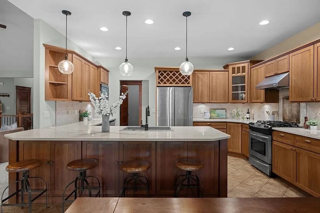 Modern kitchen with wooden cabinets, island with barstools, stainless steel appliances, and pendant lighting.