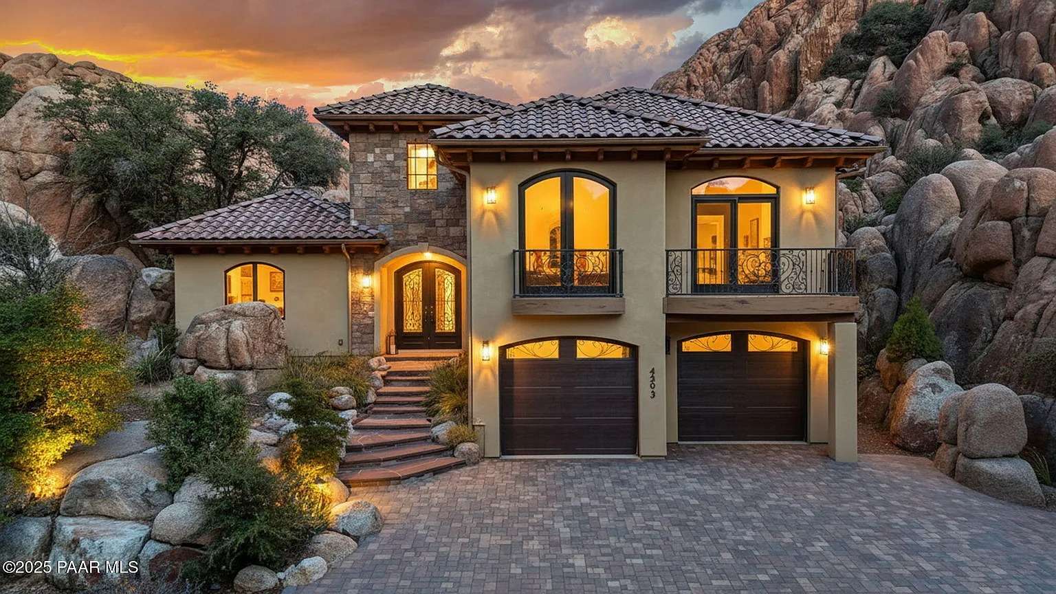 Mediterranean-style house with stone accents, arched windows, and a sunset sky backdrop.