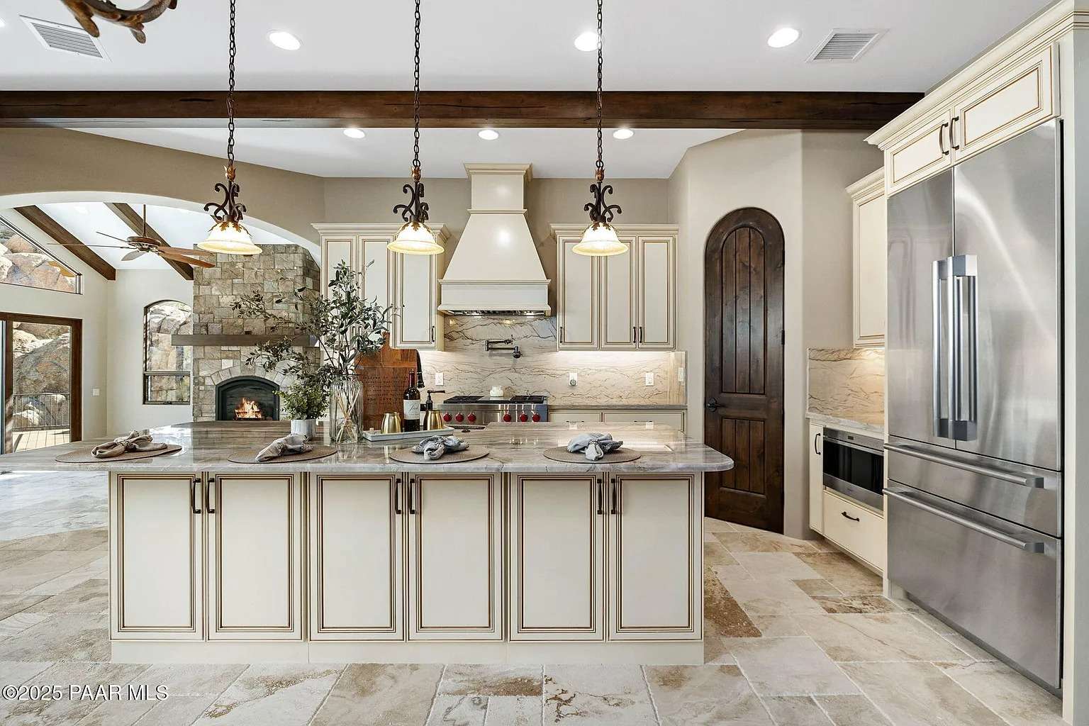 Spacious kitchen with marble island, stainless steel appliances, and rustic stone fireplace in the background.