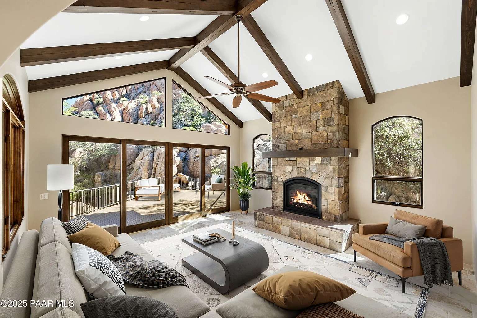 Spacious living room with vaulted ceiling, stone fireplace, and large windows overlooking rocky landscape.