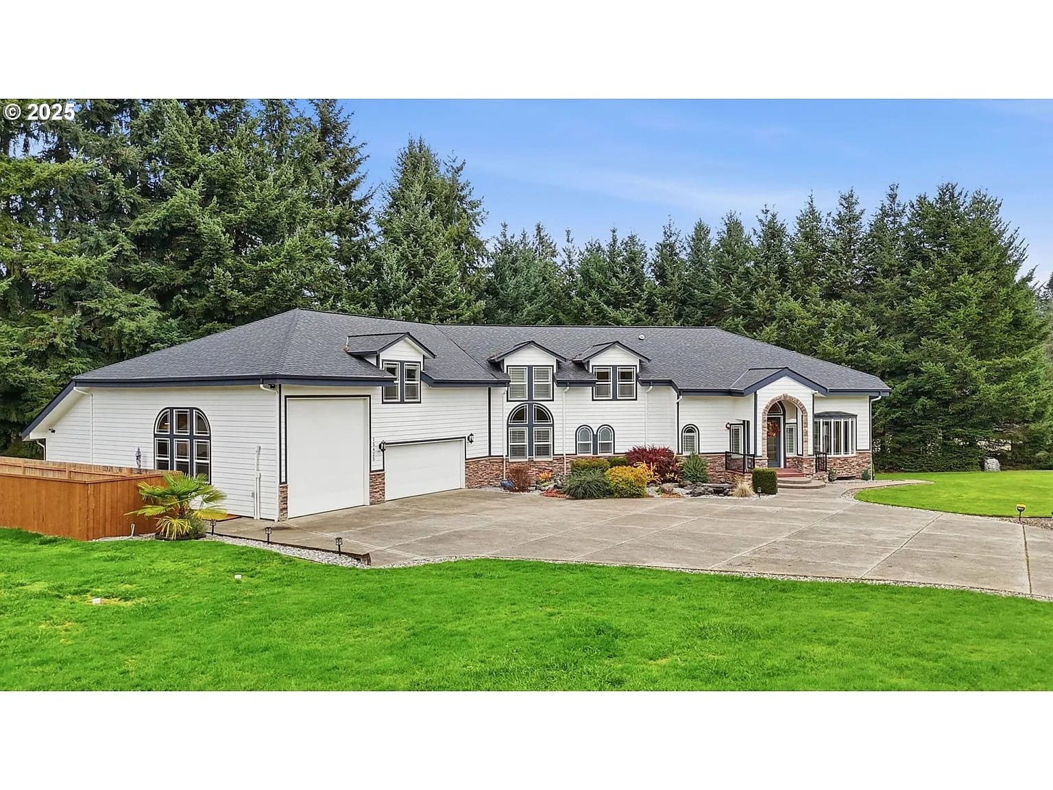 Large white house with a dark roof, surrounded by trees and a spacious driveway.