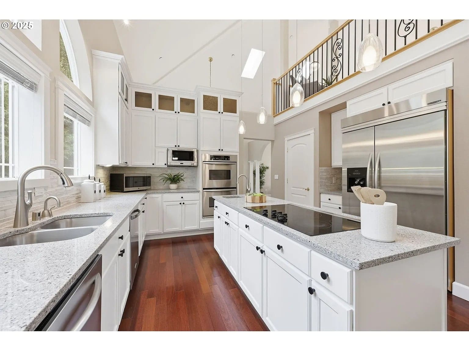 Modern kitchen with white cabinets, stainless steel appliances, granite countertops, and hardwood floors.