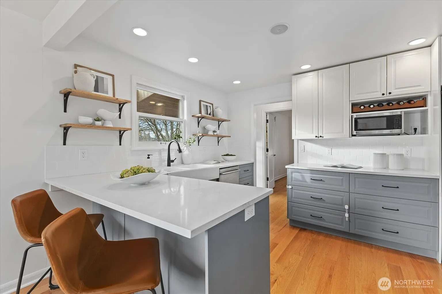 Modern kitchen with white countertops, gray cabinets, open shelves, and two brown chairs at the island.