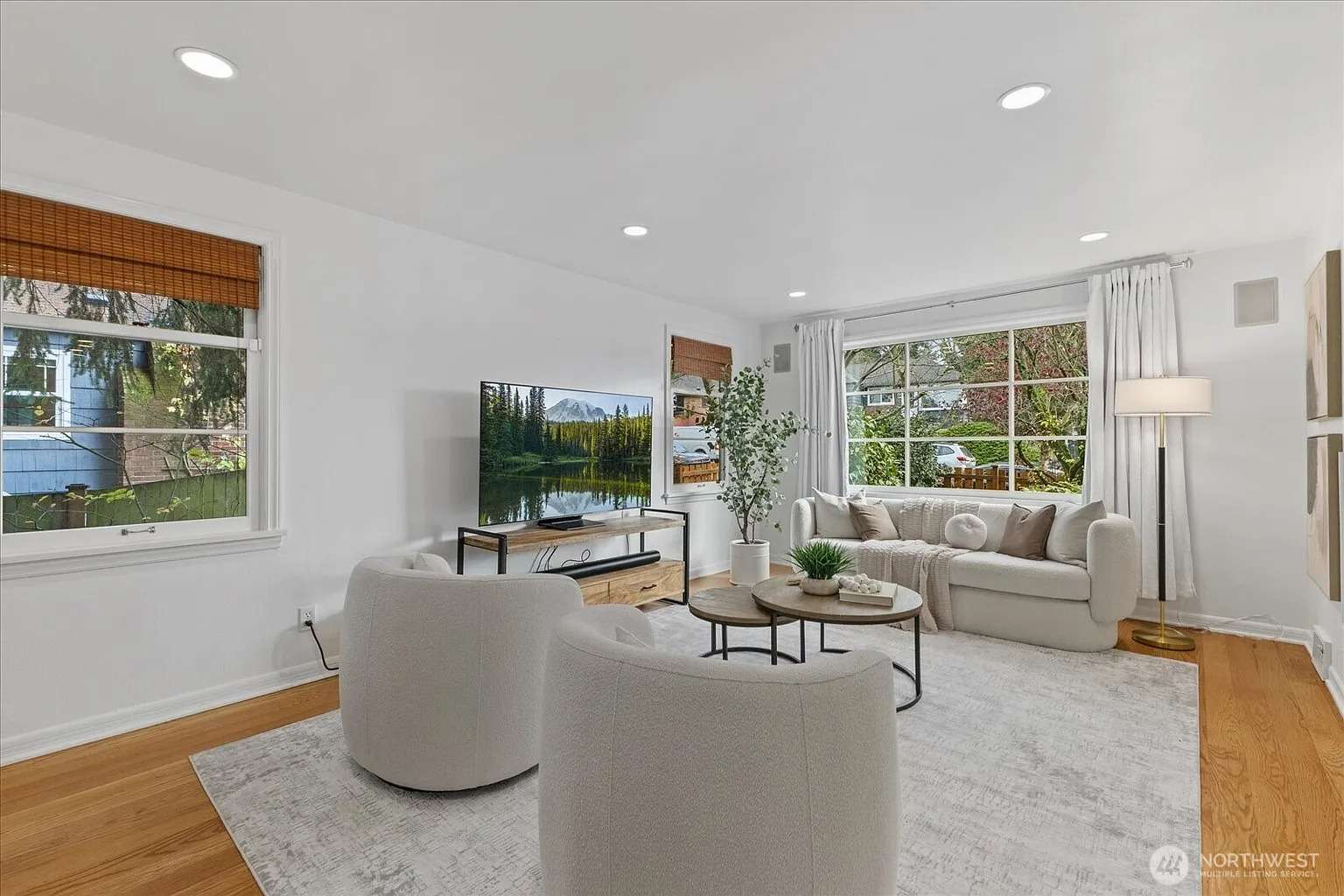 Modern living room with white walls, round chairs, a TV, and large windows with natural light.
