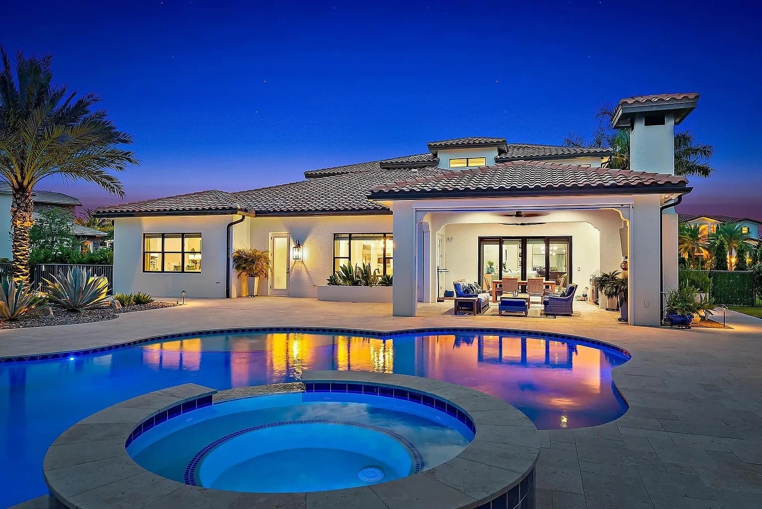 Luxurious house with a pool and hot tub, illuminated at dusk with palm trees nearby.