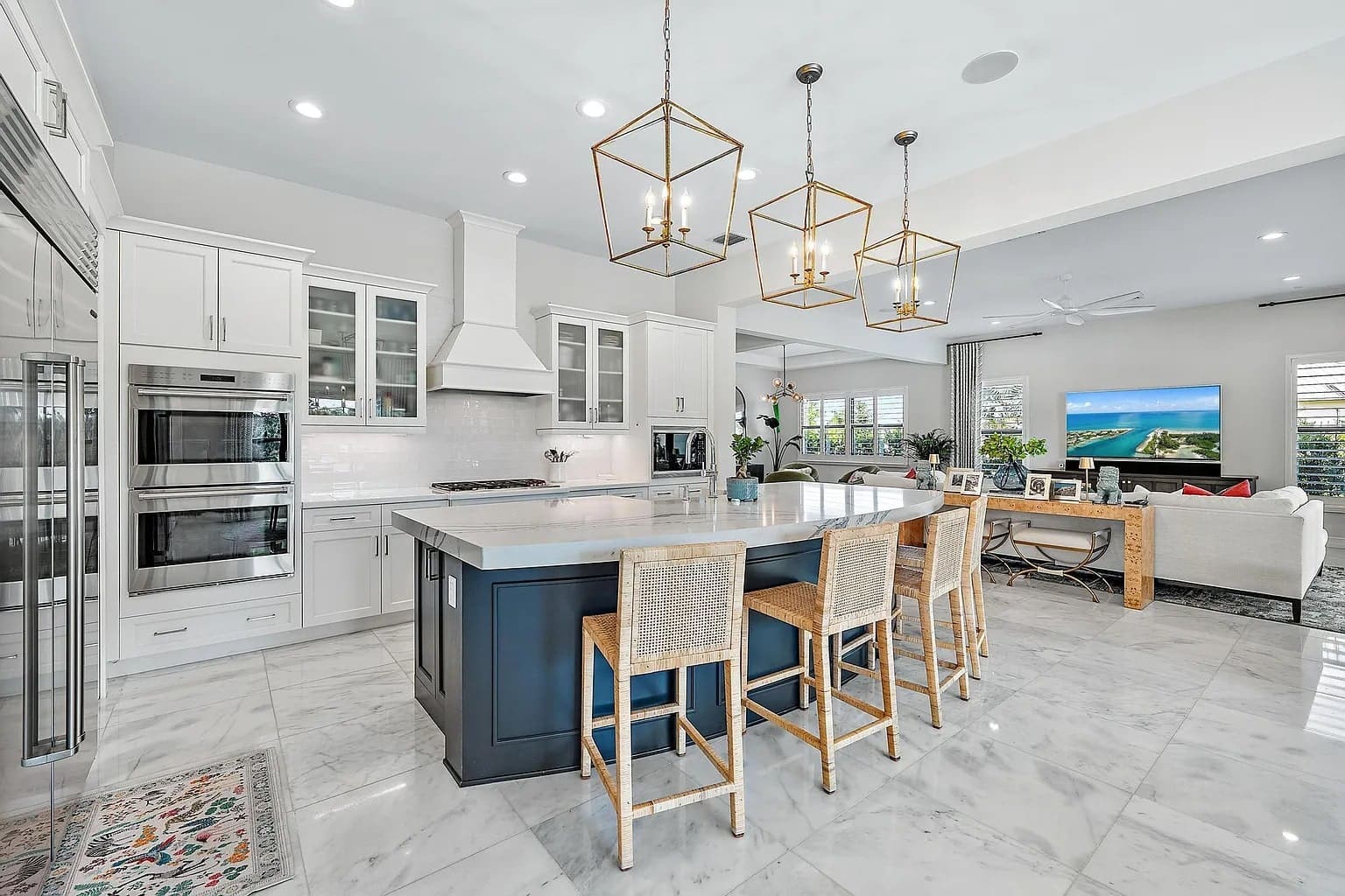 Modern kitchen with marble floors, large island, wicker chairs, and open living area with a TV.