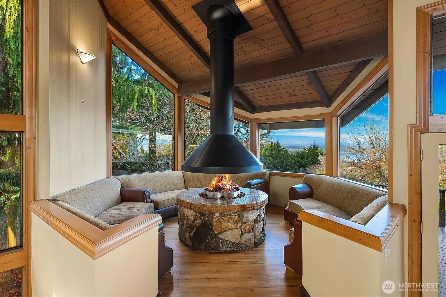 Cozy room with a central fireplace, surrounded by curved seating and large windows.