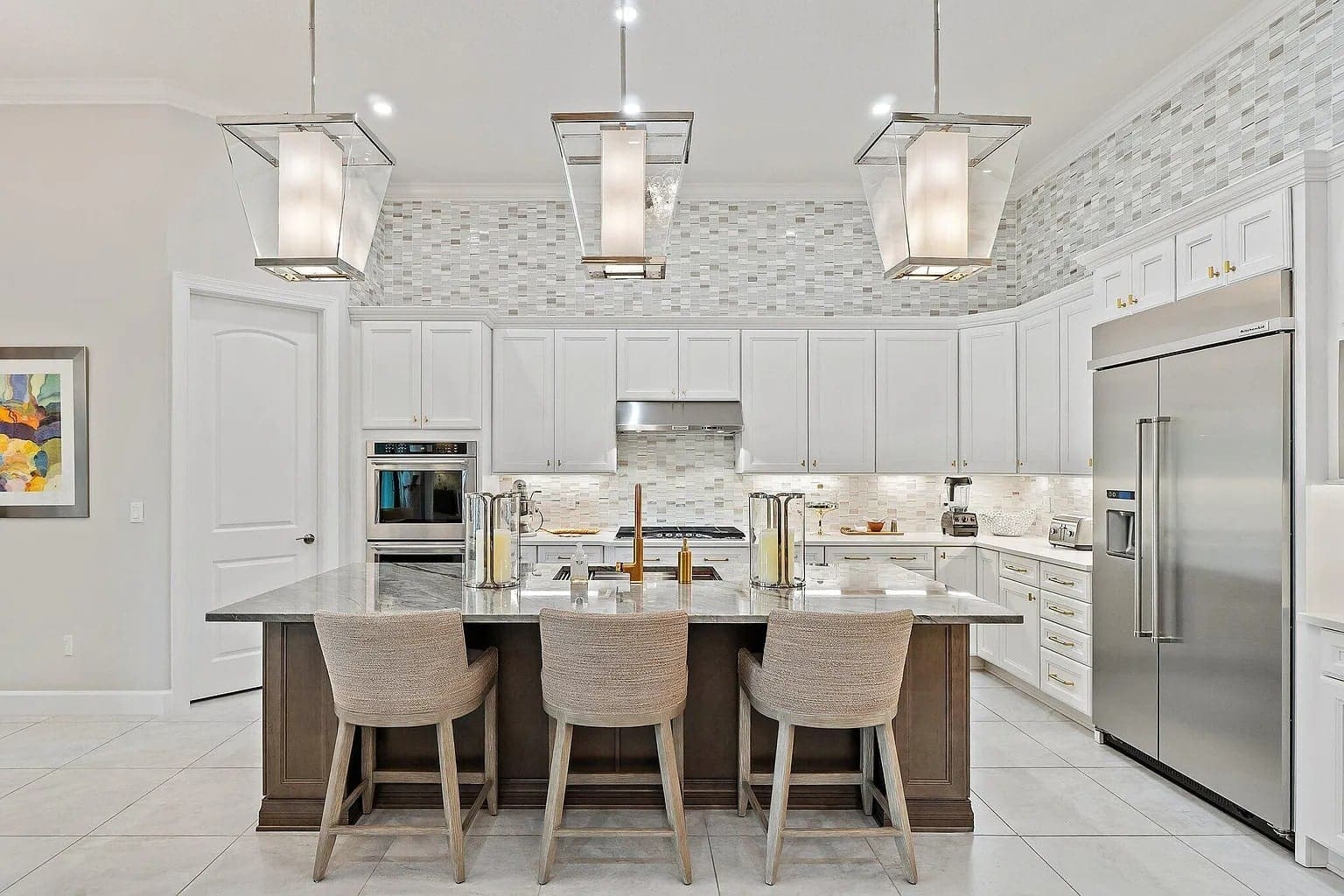 Modern kitchen with white cabinets, large island, three chairs, and stainless steel appliances.
