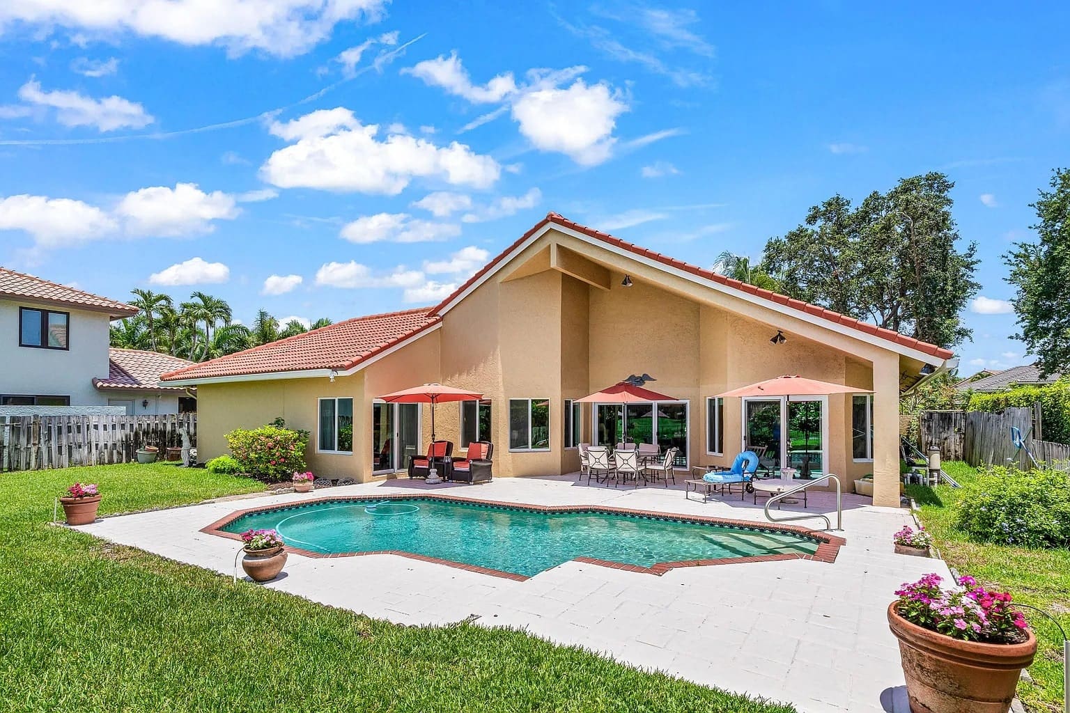 Backyard with a swimming pool, patio furniture, and a beige house under a clear blue sky.