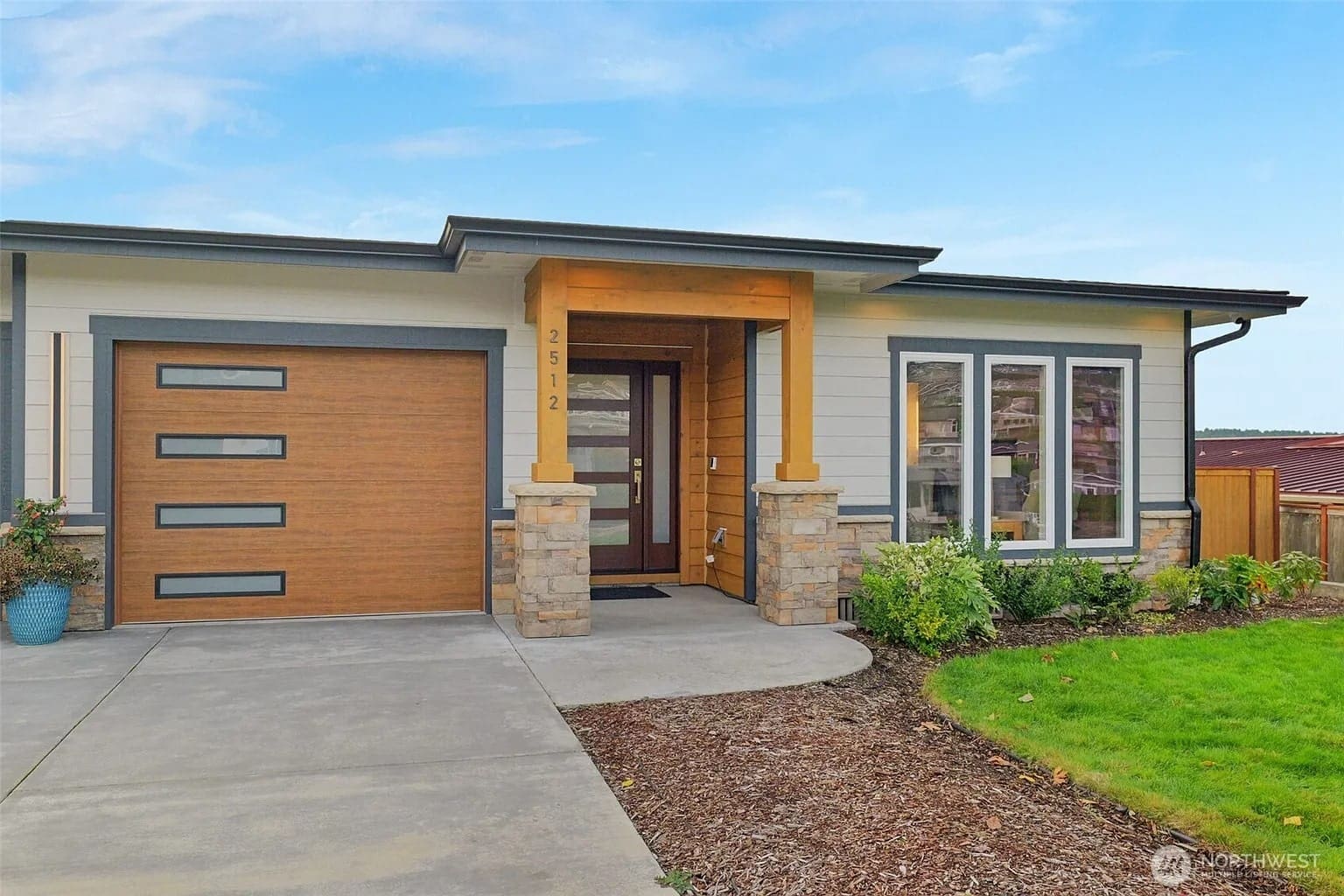 Modern single-story house with wooden accents, large garage door, and landscaped front yard.