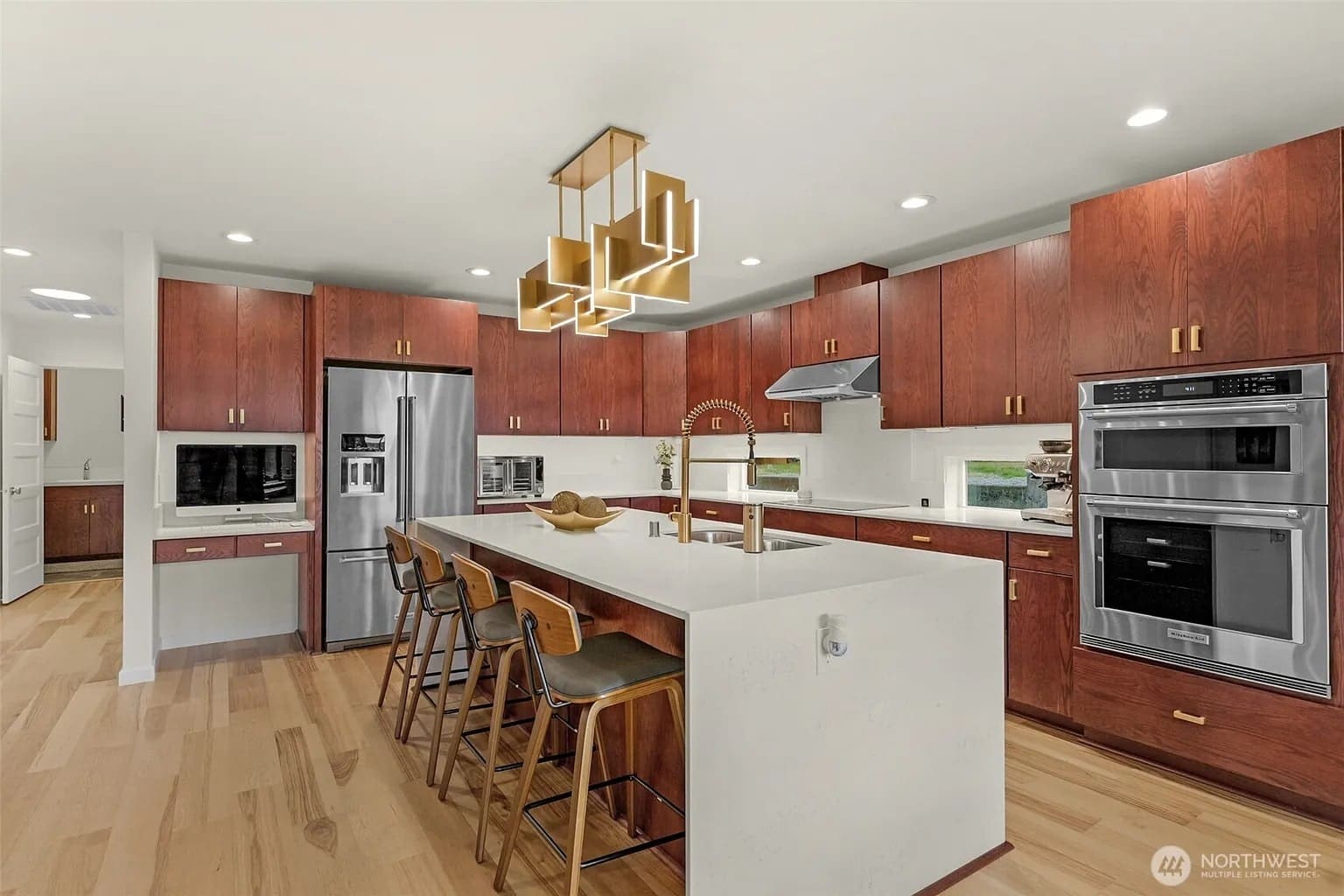 Modern kitchen with wooden cabinets, island with bar stools, stainless steel appliances, and geometric light fixture.