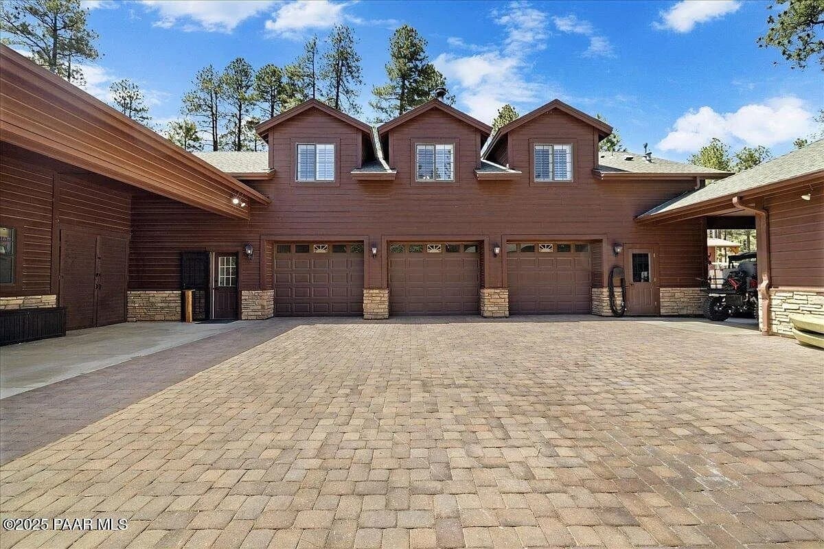 Large brown house with three garage doors and a spacious paved driveway.