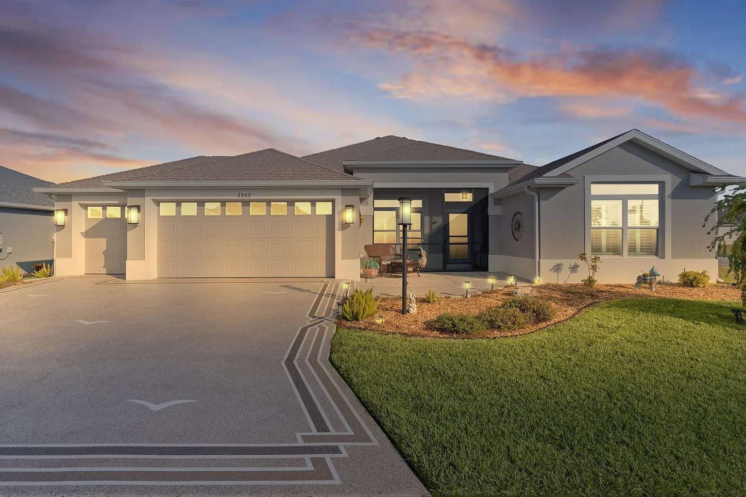 Modern single-story house with a two-car garage, landscaped yard, and sunset sky background.