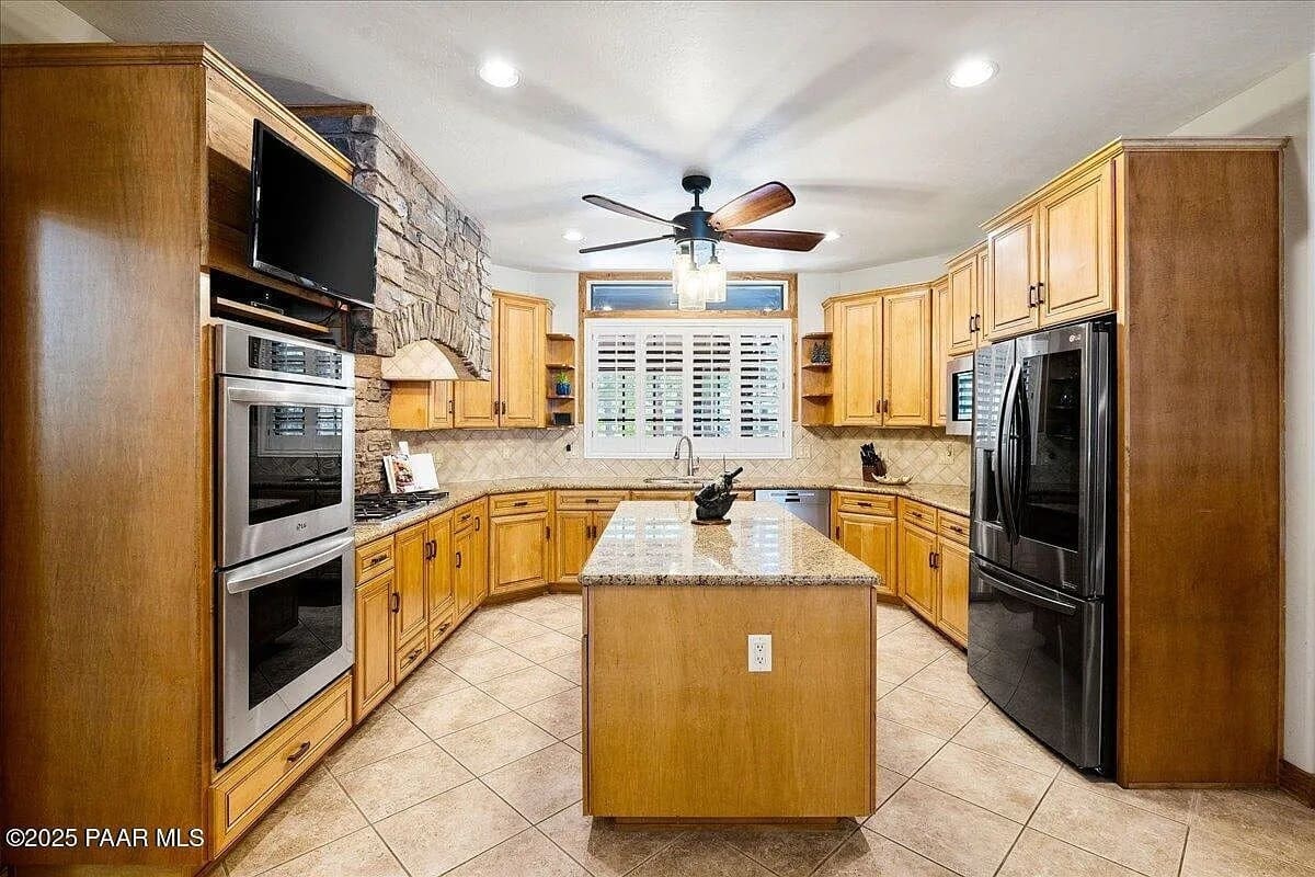 Spacious kitchen with wooden cabinets, stone accent wall, island, and stainless steel appliances.