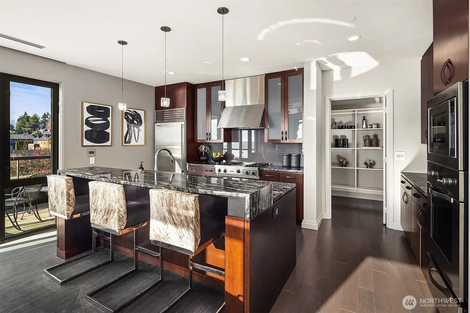 Modern kitchen with dark wood cabinets, marble island, stainless steel appliances, and fur-covered bar stools.
