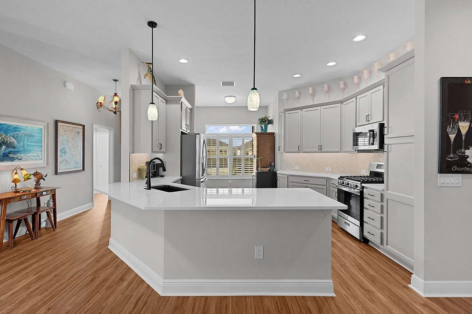 Modern kitchen with white cabinets, stainless steel appliances, and a large island with pendant lights.
