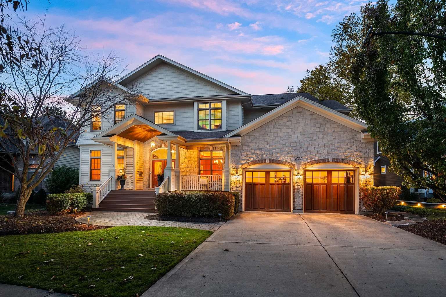 Two-story house with stone facade, warm lighting, and a double garage at sunset.