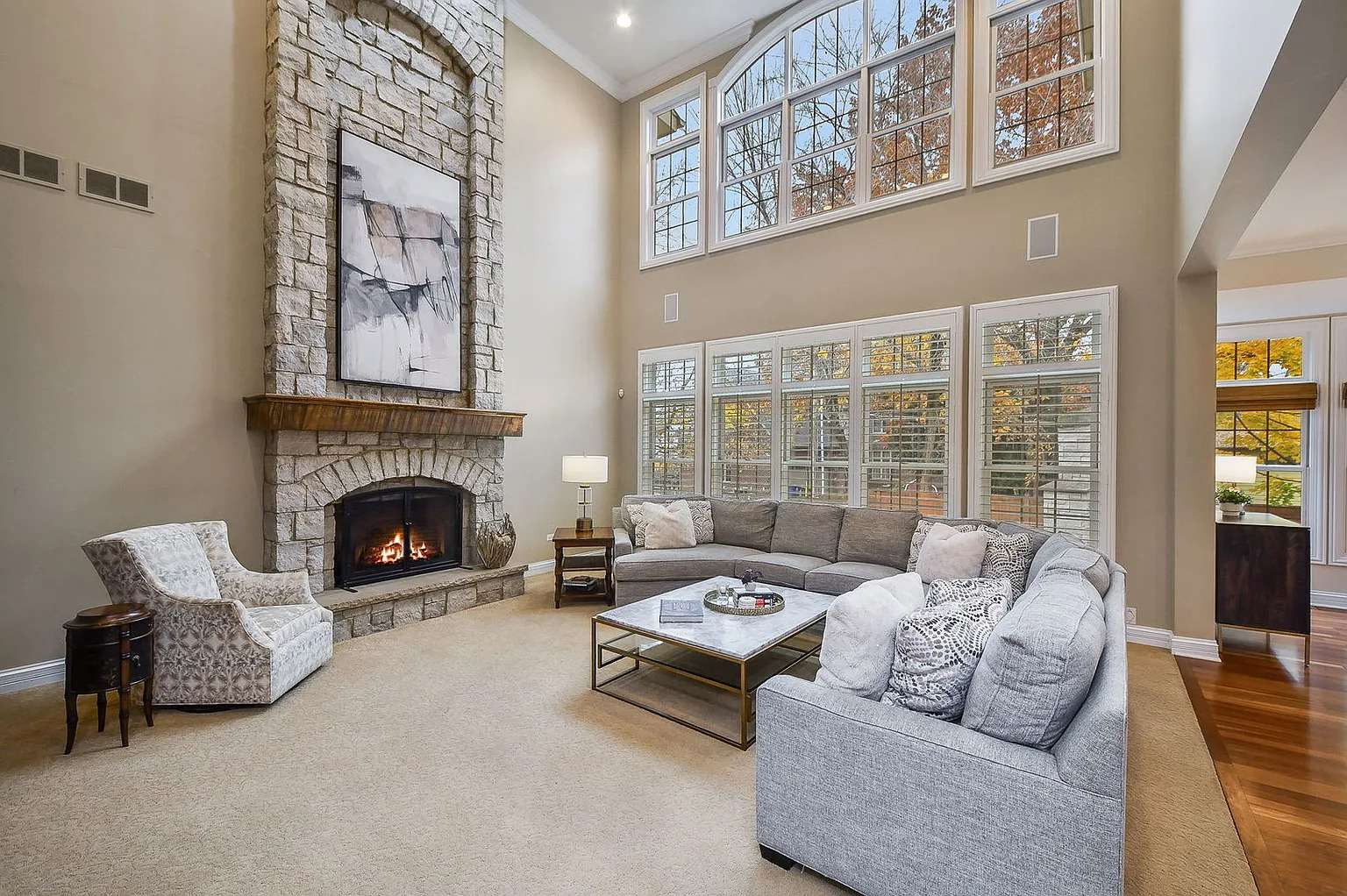 Spacious living room with high ceilings, large windows, stone fireplace, and gray sectional sofa.